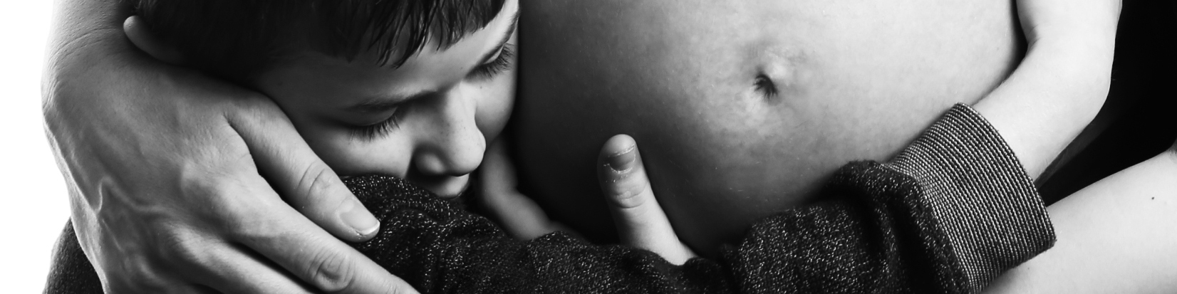 Black and white photograph of a child hugging his mother's pregnant tummy